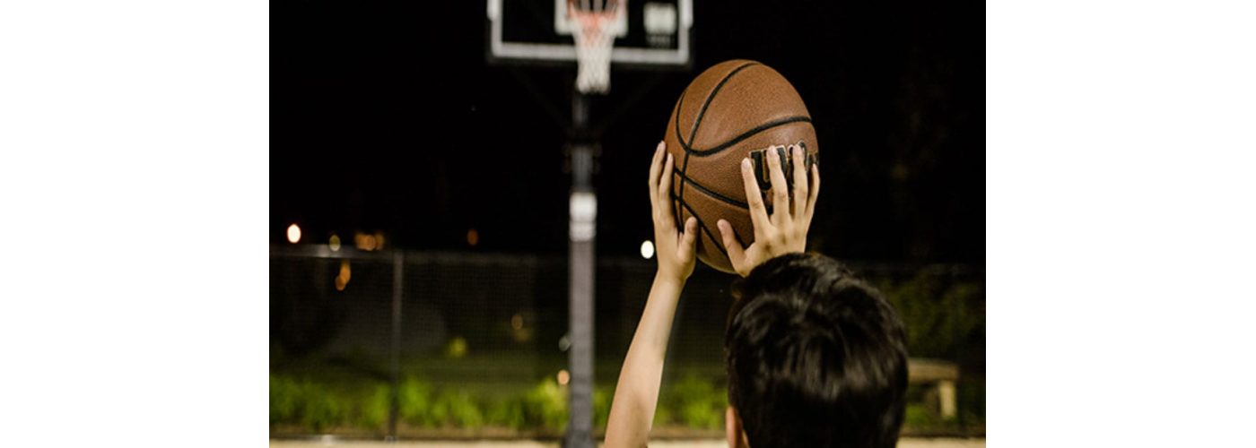 A person playing basketball at night with court lights on