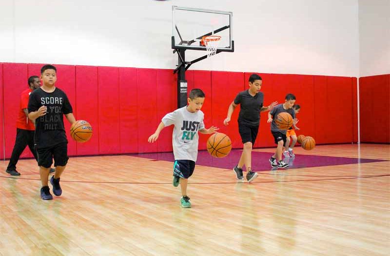 Children dribbling basketballs down a basketball court